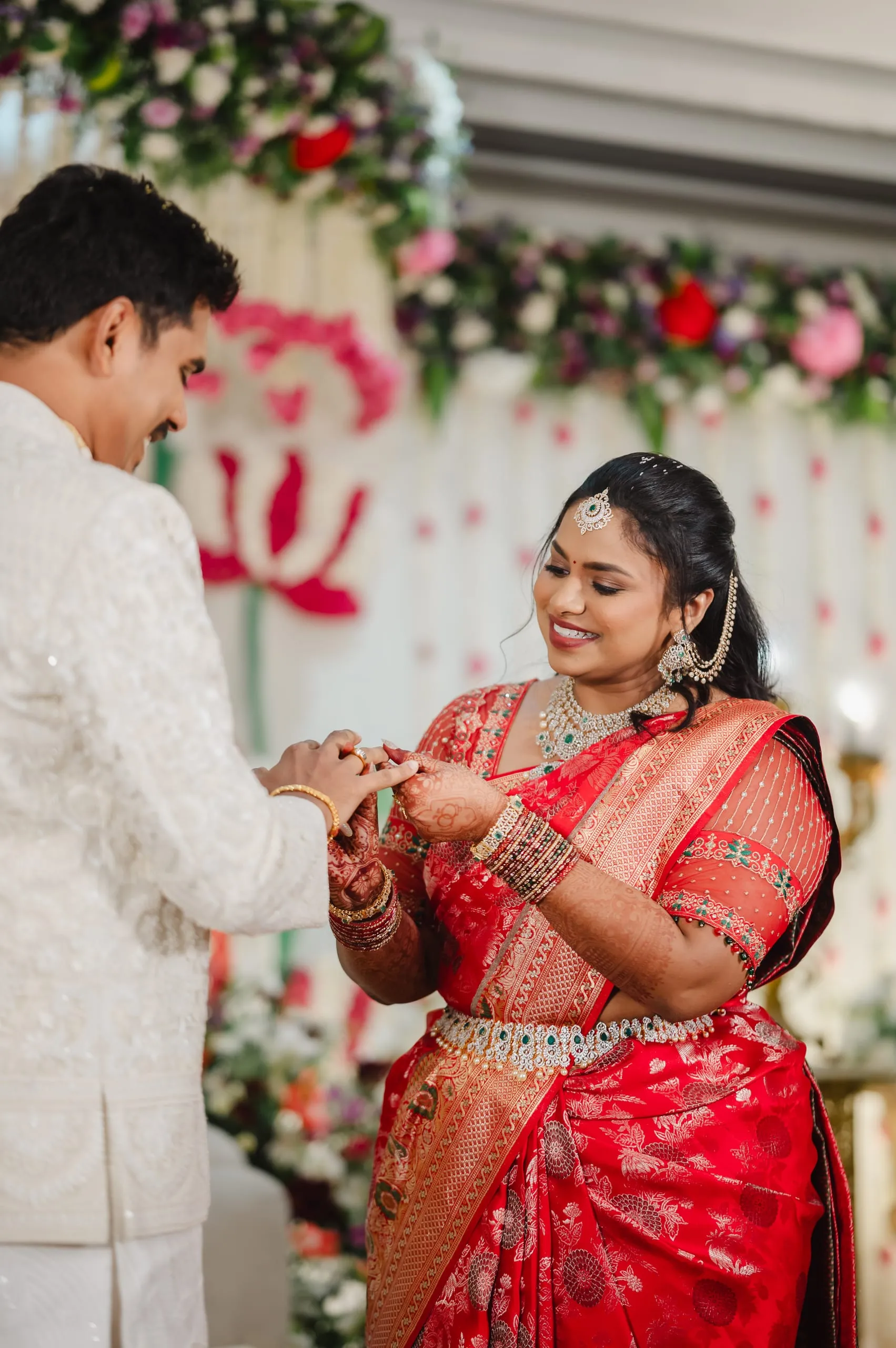 Swathi and Gautham exchanging rings before a floral backdrop